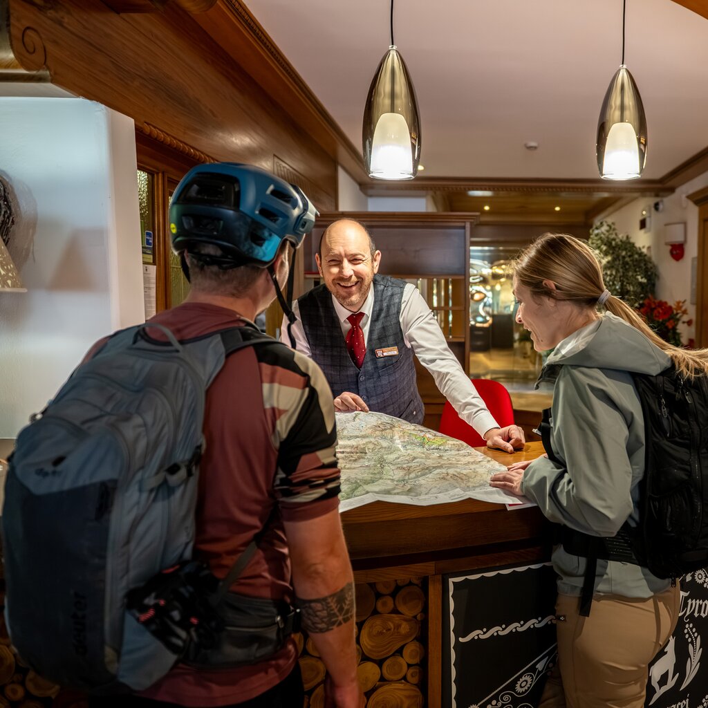 Un receptionist consiglia due biker su quali percorsi seguire, all'interno di un hotel | © Andrea Costa - Archivio immagini ApT Val di Fassa