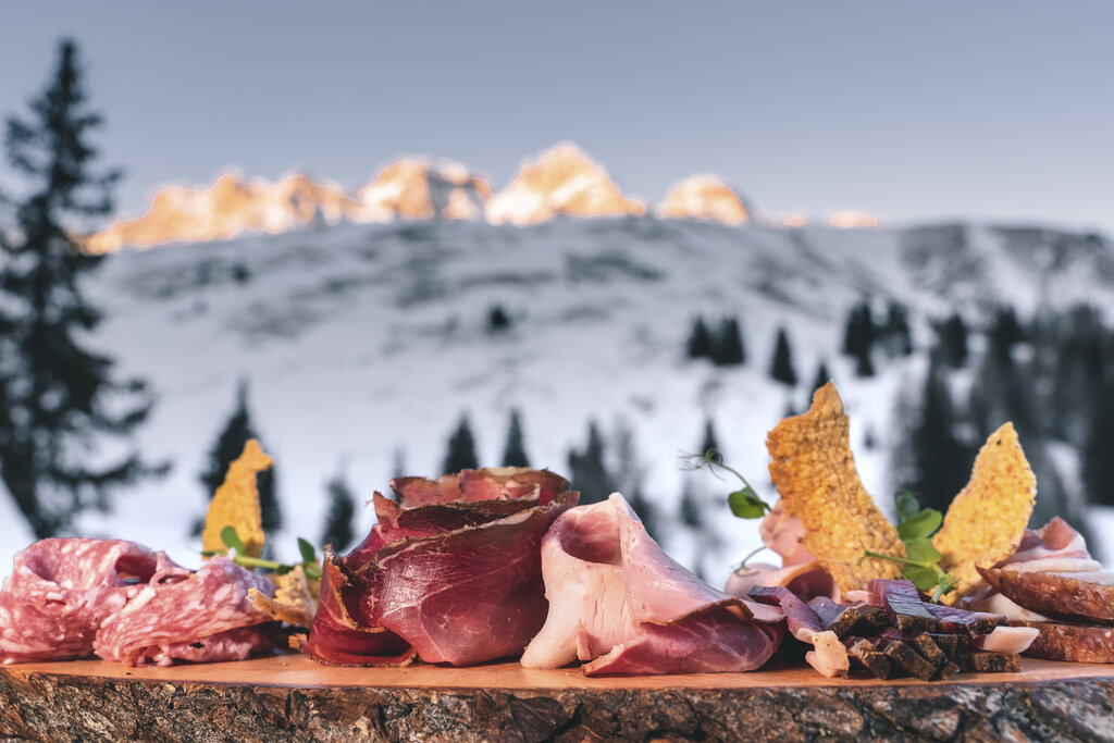 Tagliere di salumi e formaggi della Val di Fassa con sfondo le Dolomiti