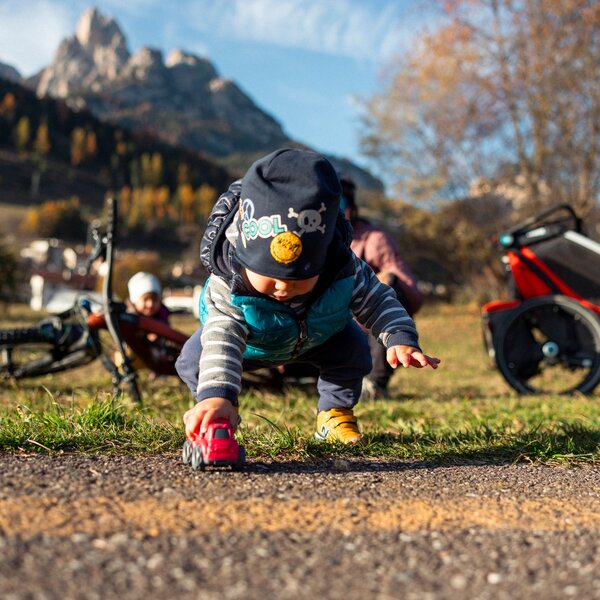 Bambino che gioca lungo la pista ciclopedonale di Pozza-Pera con una macchinina all'aperto in Val di Fassa, con il Larsec sullo sfondo | © Archivio immagini ApT Val di Fassa - Federico Modica