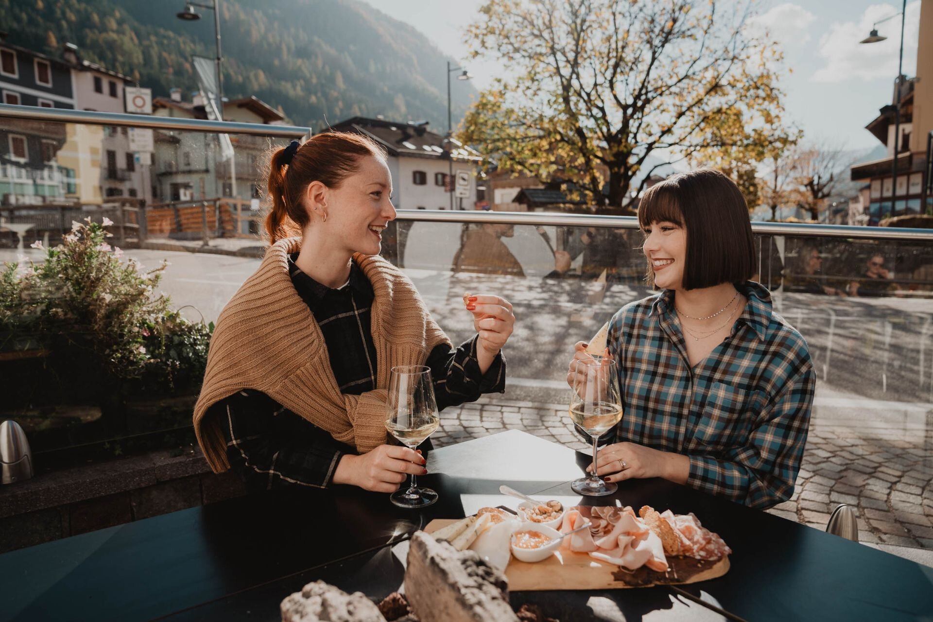 Coppia di ragazze brinda e mangia da un tagliere con prodotti tipici della Val di Fassa | © Archivio immagini ApT Val di Fassa - Mattia Rizzi