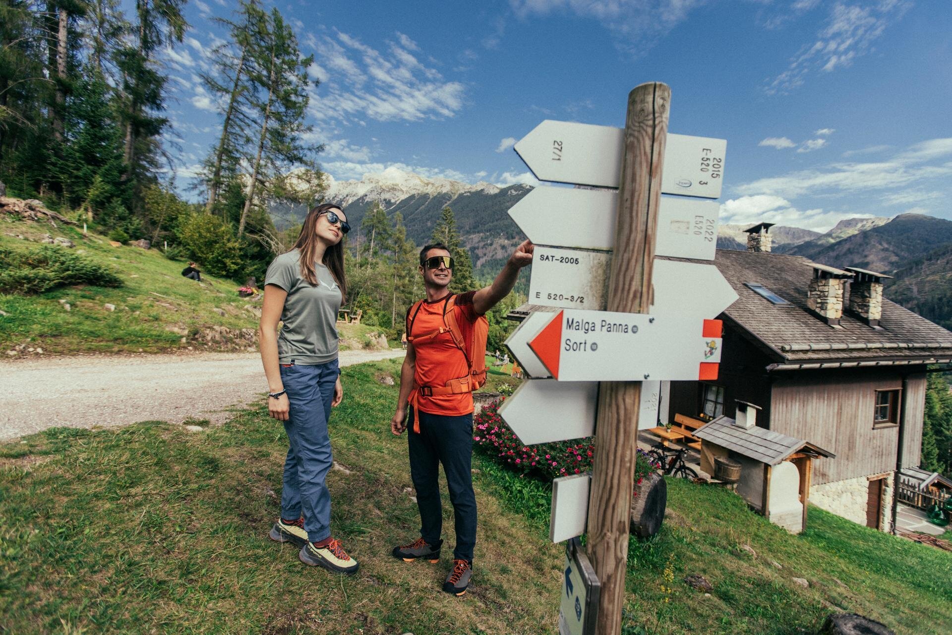 Una coppia ossrva i cartelli con le indicazioni delle località per delle camminate, sullo sfondo, le Dolomiti | © Archivio Immagini ApT Val di Fassa - Federico Modica