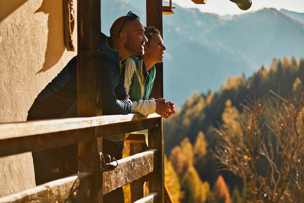 Persone che ammirano il paesaggio della Val di Fassa in autunno da una baita in legno