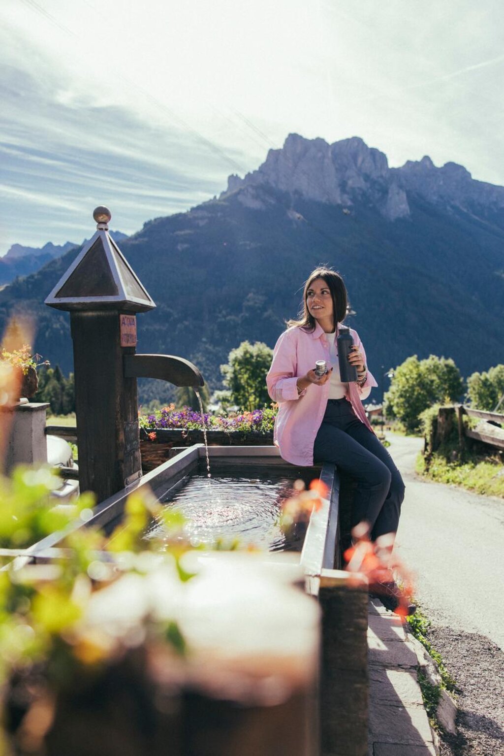 Ragazza siede sul bordo di una fontana con una borraccia in mano