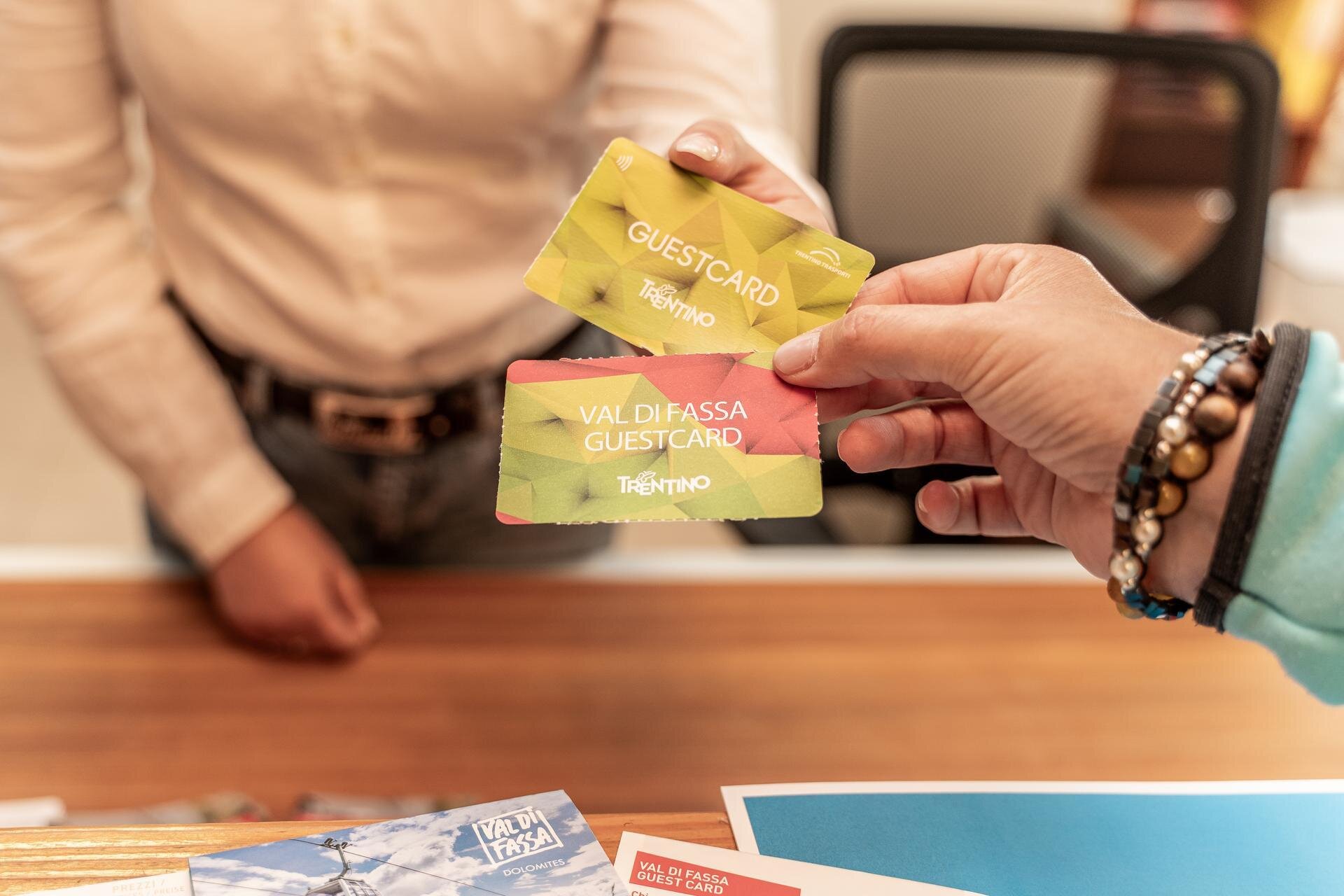 Primo piano di due mani che tengono la trentino guest card e la val di fassa guest card, in carta colorata | © Archivio Immagini ApT Val di Fassa - Patricia Ramirez