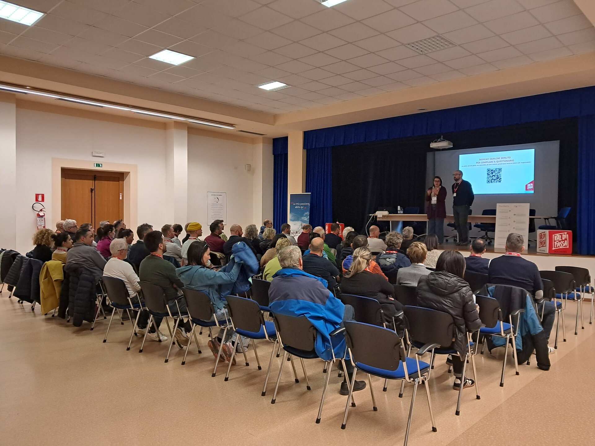 Assemblea di persone sedute su sedie davanti ad un palco | © ApT Val di Fassa