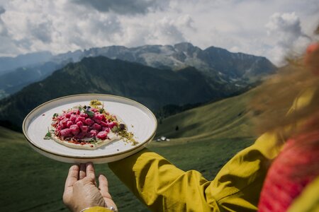 Piatto di cucina ladina, sullo sfondo le Dolomiti della Val di Fassa