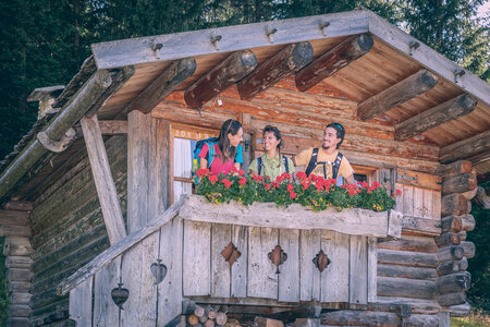 Persone affacciate su un balcone in fiore di una baita in Val di Fassa