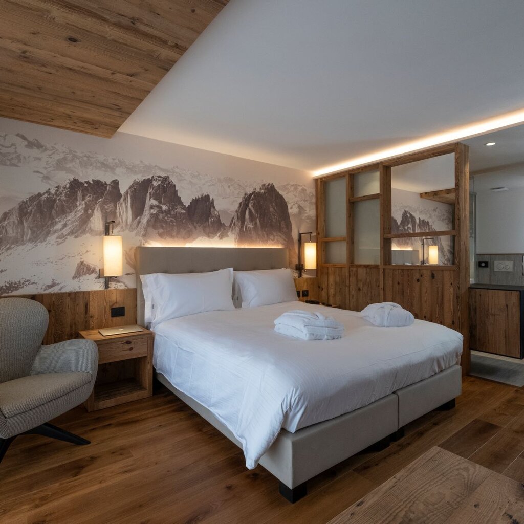 Camera di hotel arredata in legno con fotografia delle Dolomiti sullo sfondo | © Archivio Immagini ApT Val di Fassa