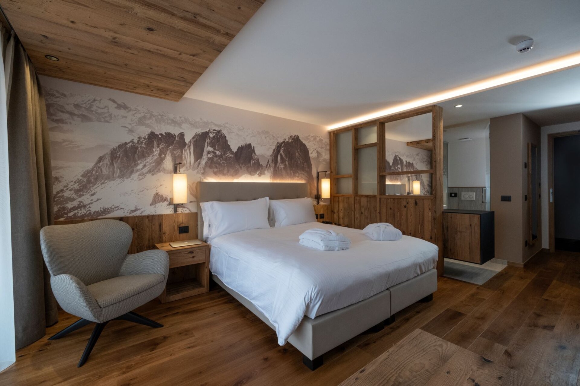 Camera di hotel arredata in legno con fotografia delle Dolomiti sullo sfondo | © Archivio Immagini ApT Val di Fassa